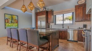 A kitchen with wooden cabinets, a stainless steel refrigerator, and a dining area with striped chairs. - Escape to Cabo Luxury at Las Terrazas #05 (Cabo San Lucas)