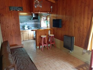 A wooden interior with a kitchen area, a bar stool, a television, and a bed.