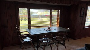 A dining area with a wooden table and chairs, large windows with blinds, and a view of the outside. - Lakeshore Cottage, For Outdoor Enthusiasts (Gaylord)