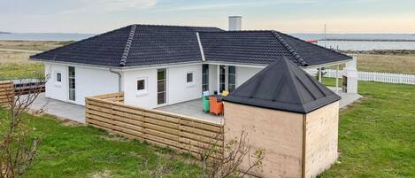 Ein modernes Haus mit einer großen Terrasse, einem überdachten Sitzbereich im Freien und Blick aufs Meer.