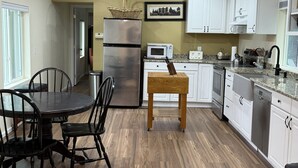 Une cuisine moderne avec un coin repas, un plancher en bois, des armoires blanches et un réfrigérateur en acier inoxydable.