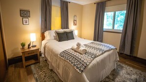 Une chambre à coucher avec un lit, une table de chevet, un ventilateur de plafond et une fenêtre avec des rideaux.