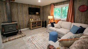 Un salon avec une cheminée, un canapé, un téléviseur et une fenêtre avec des rideaux.