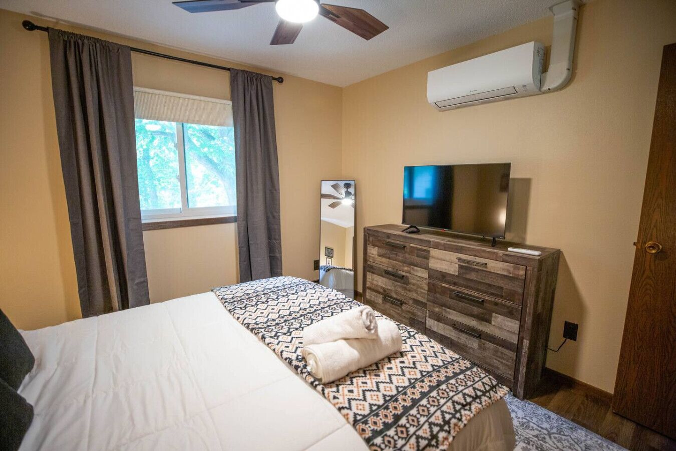 A hotel room with a bed, a dresser, a television, and an air conditioning unit.