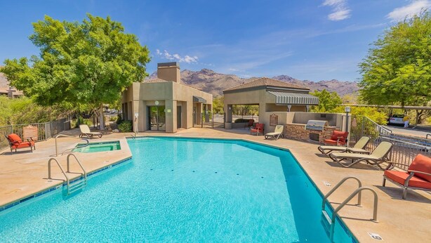 A swimming pool with lounge chairs and a barbecue area, surrounded by trees and mountains in the background.