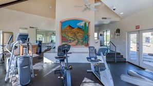 A gym with stationary bikes, a ceiling fan, and a mural of a desert landscape.