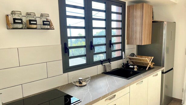 Une cuisine moderne dotée d’une plaque de cuisson à induction noire, d’un réfrigérateur en acier inoxydable et d’une fenêtre à carreaux multiples.