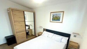 Une chambre à coucher avec un grand lit, une armoire avec un miroir, une table de chevet et une petite étagère à côté du lit.