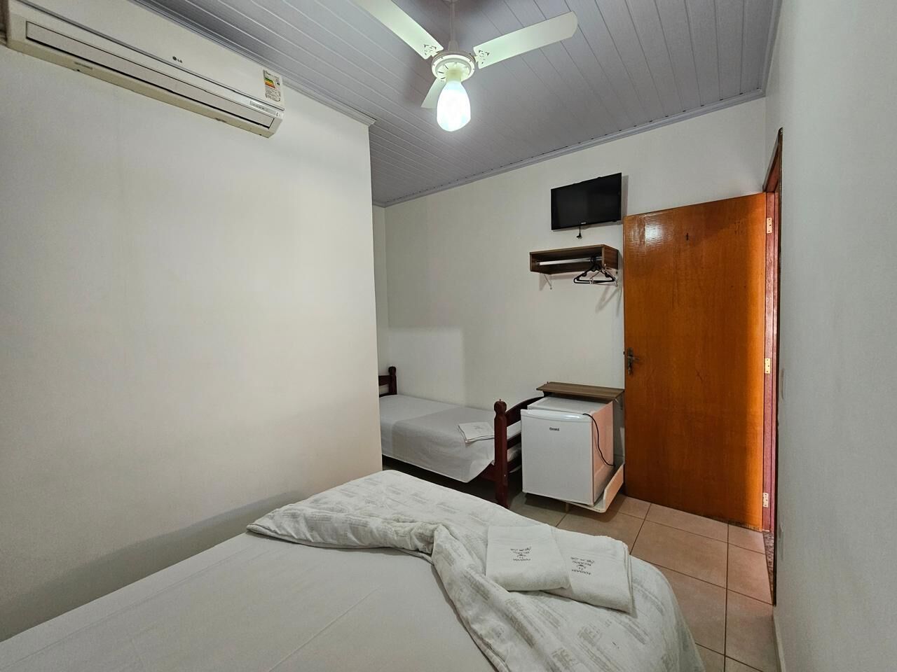 A small, clean room with a bed, a desk, a chair, a wardrobe, and a ceiling fan.