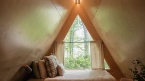 Ein gemütliches Schlafzimmer im Dachgeschoss mit schrägen Wänden, einem Bett mit Kissen, einem kleinen Tisch und einem Stuhl.