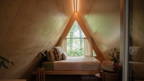 Ein gemütlicher, dreieckiger Raum mit einem Bett, einem kleinen Tisch und einem Fenster mit Blick auf Grünflächen.