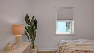 A bedroom with a bed, a bedside table with a lamp, a potted plant, and a window.