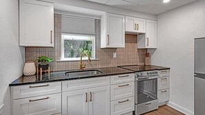 Une cuisine moderne avec des meubles blancs, un plan de travail noir et une fenêtre équipée de stores.