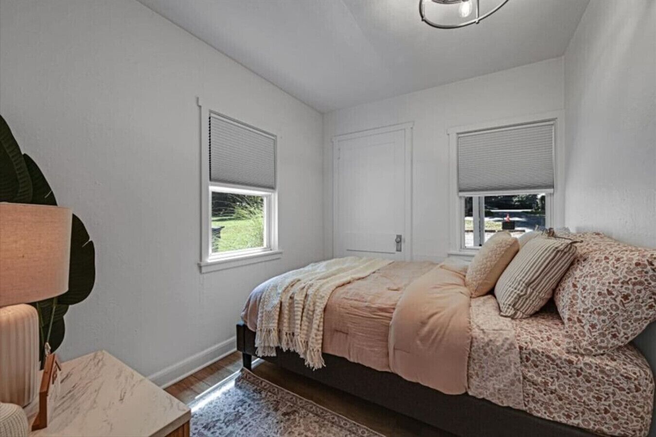 A bedroom with a bed, two windows with blinds, a lamp, and a rug.