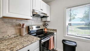 A kitchen with white cabinets, a granite countertop, a stainless steel stove, and a window with blinds.