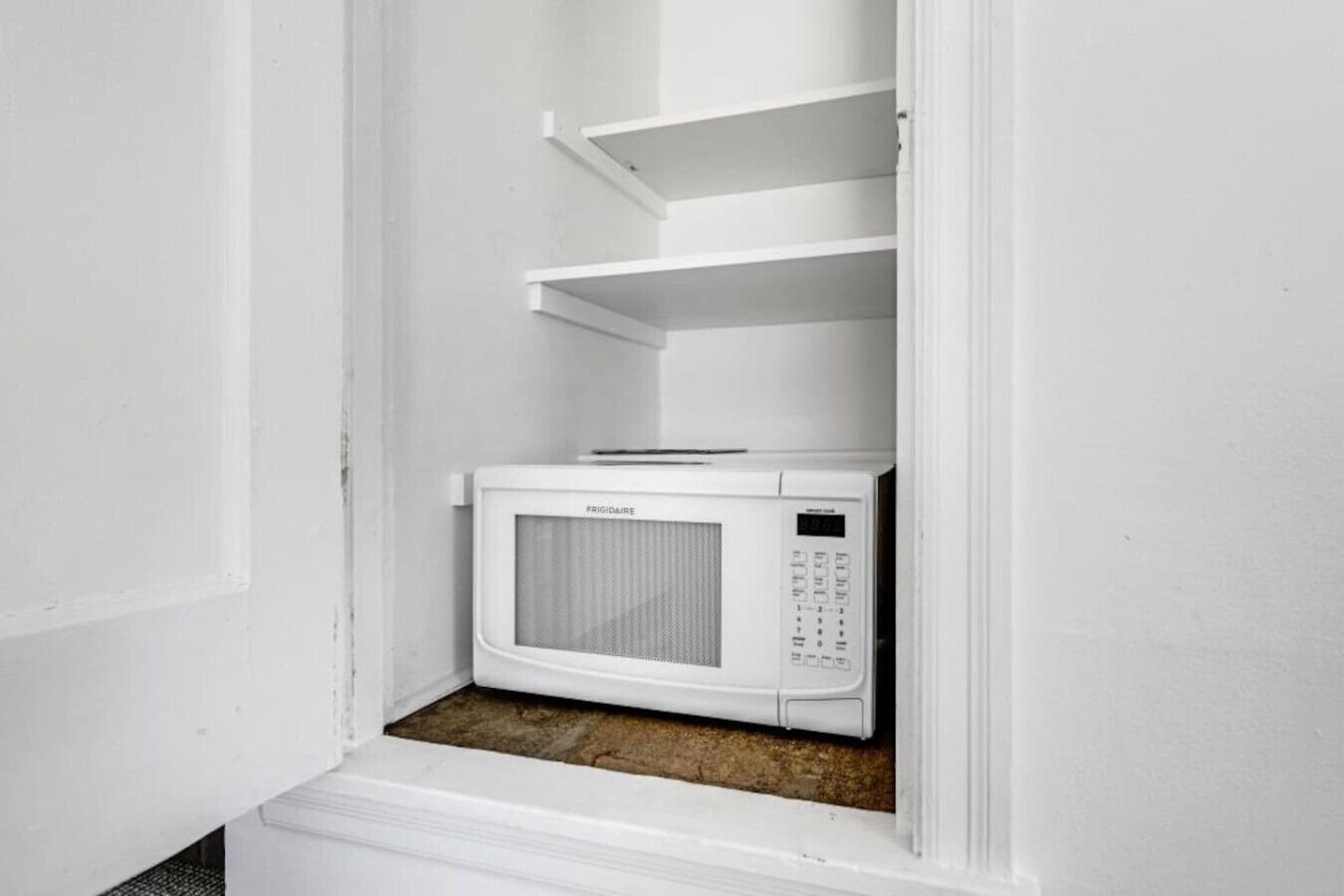 A white microwave in a corner with a shelf above it.