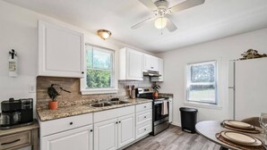 A modern kitchen with white cabinets, a granite countertop, a built-in oven, and a ceiling fan.