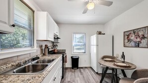 A compact kitchen with granite countertops, a double sink, a ceiling fan, and a dining area with a table and chairs.
