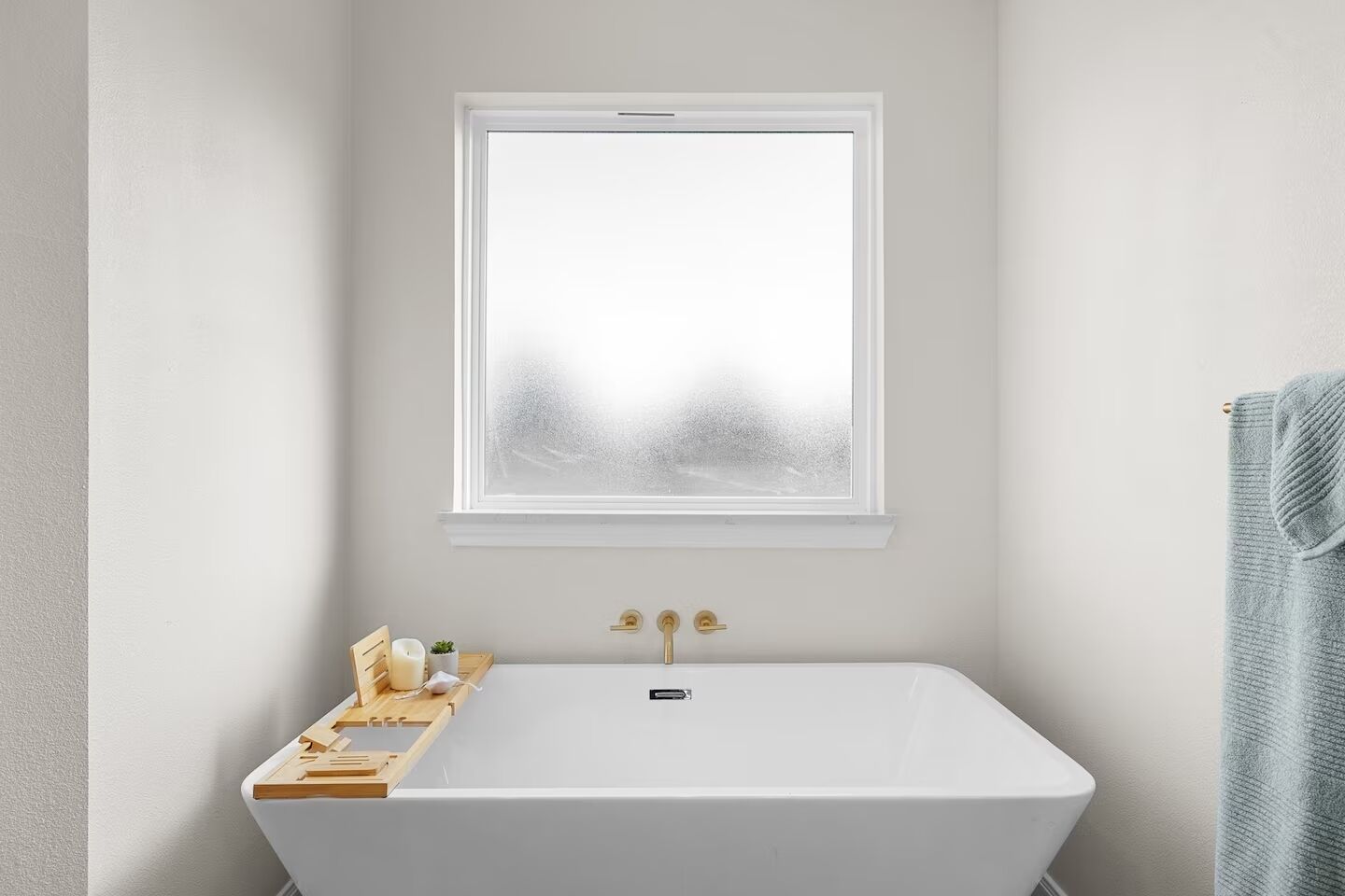 Ein Badezimmer mit einer weißen Badewanne, einem Fenster mit Milchglas und einem Handtuch an der Wand.