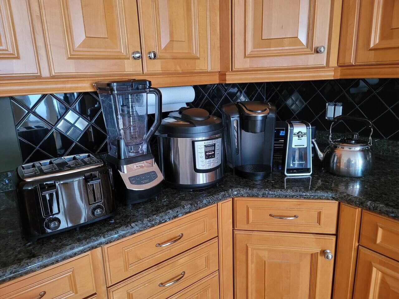 Una cocina con armarios de madera, encimera de granito, tostadora, licuadora, cocedor de arroz, cafetera y hervidor.