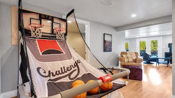 A basketball court with a net, two basketball hoops, and a slide. There is a couch and a chair in the background.