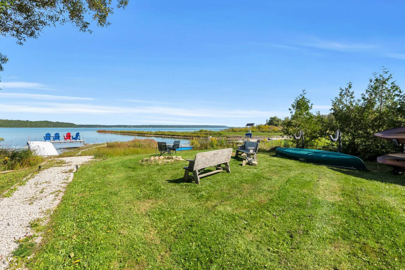 A grassy area with a bench, a small dock with chairs, and a green boat.