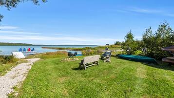 A grassy area with a bench, a small dock with chairs, and a green boat.