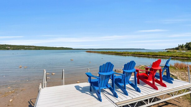 A wooden dock with blue and red Adirondack chairs facing a calm lake. - Scenic Waterfront 4BR – Hot Tub/Sleeps 12/Bonfire (Wiarton)