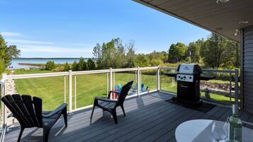 A deck with a view of a lake, a grill, and outdoor seating.