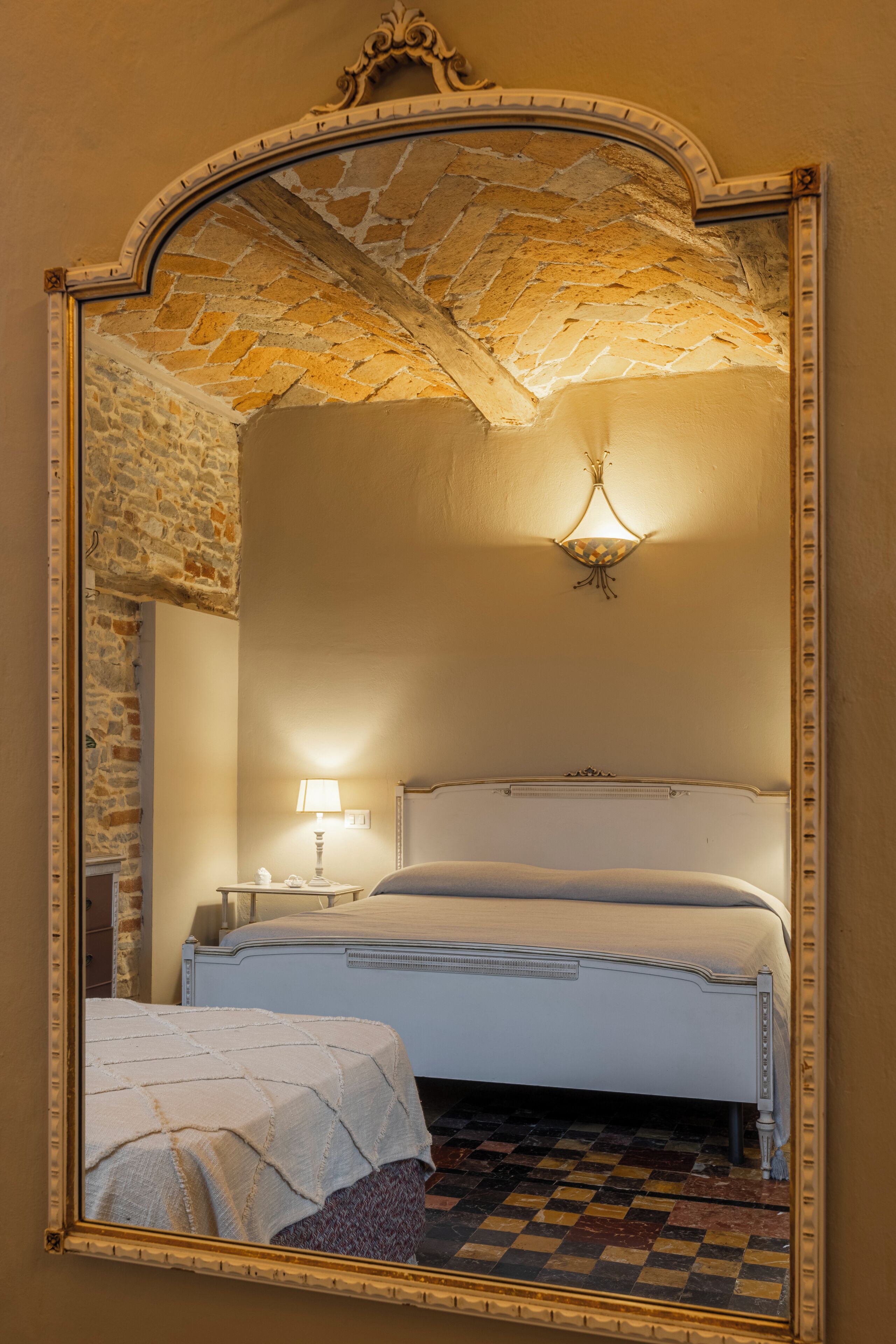 A bedroom with a large mirror, a bed, a nightstand, and a wall-mounted light fixture.