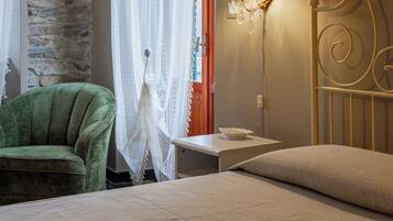 Une chambre avec un mur en pierre, un fauteuil vert, un lit avec un oreiller beige et une table de chevet avec une lampe.