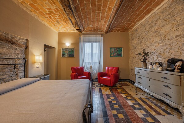 A bedroom with a brick ceiling, a checkered floor, a bed, a nightstand, a dresser, and two red chairs. - Casa Levi (Bistagno)