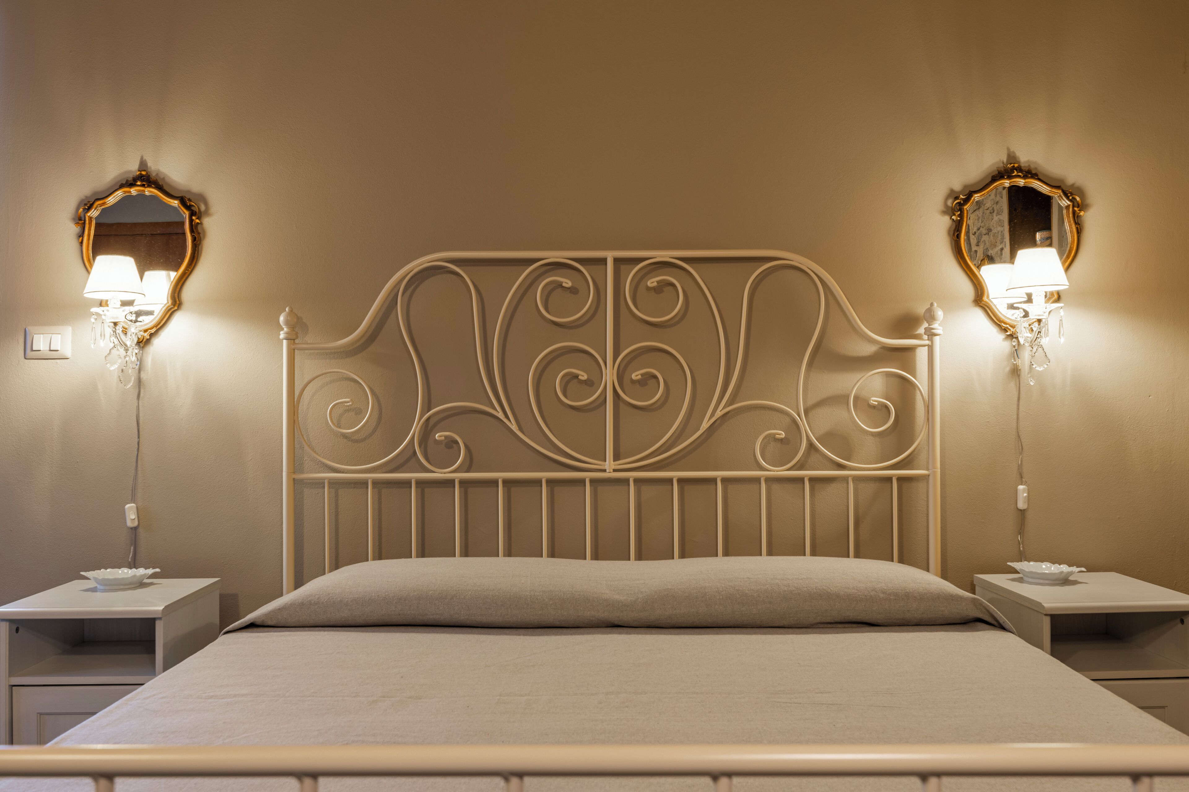 A neatly made bed with a metal headboard, two bedside tables with lamps, and wall-mounted mirrors.