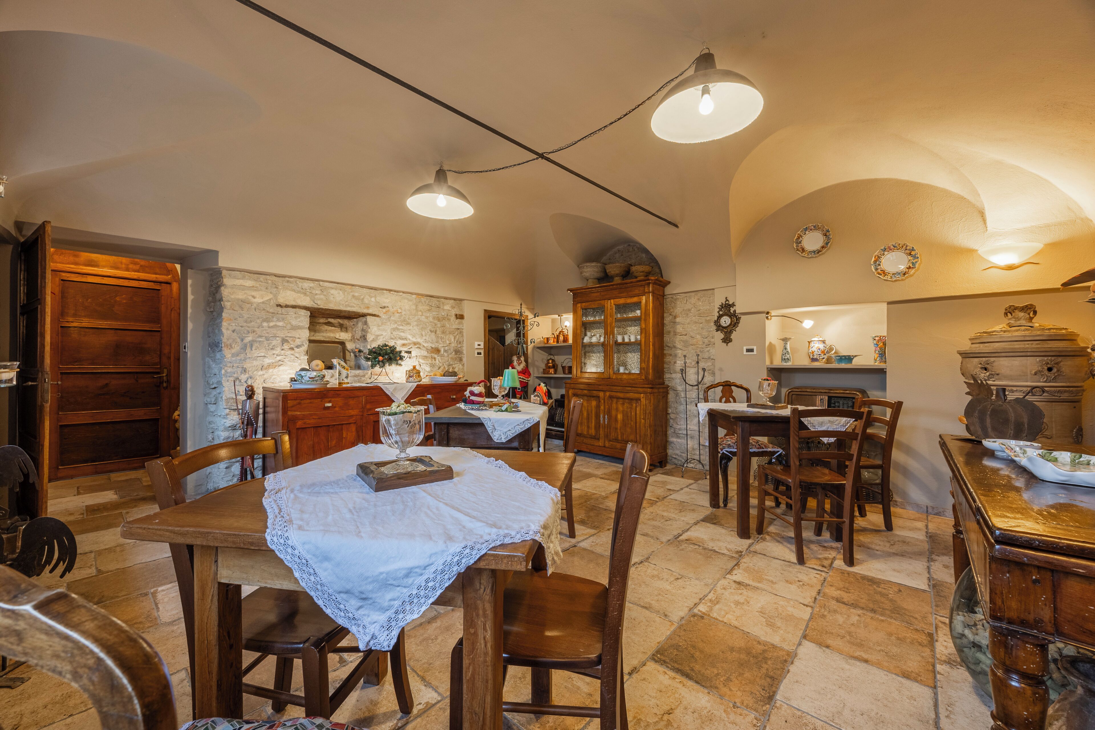 A rustic dining area with wooden tables and chairs, stone walls, and a stone fireplace.
