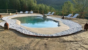 A circular pool with a pebble edge, surrounded by lounge chairs and a wooden fence. - Casa Levi (Bistagno)
