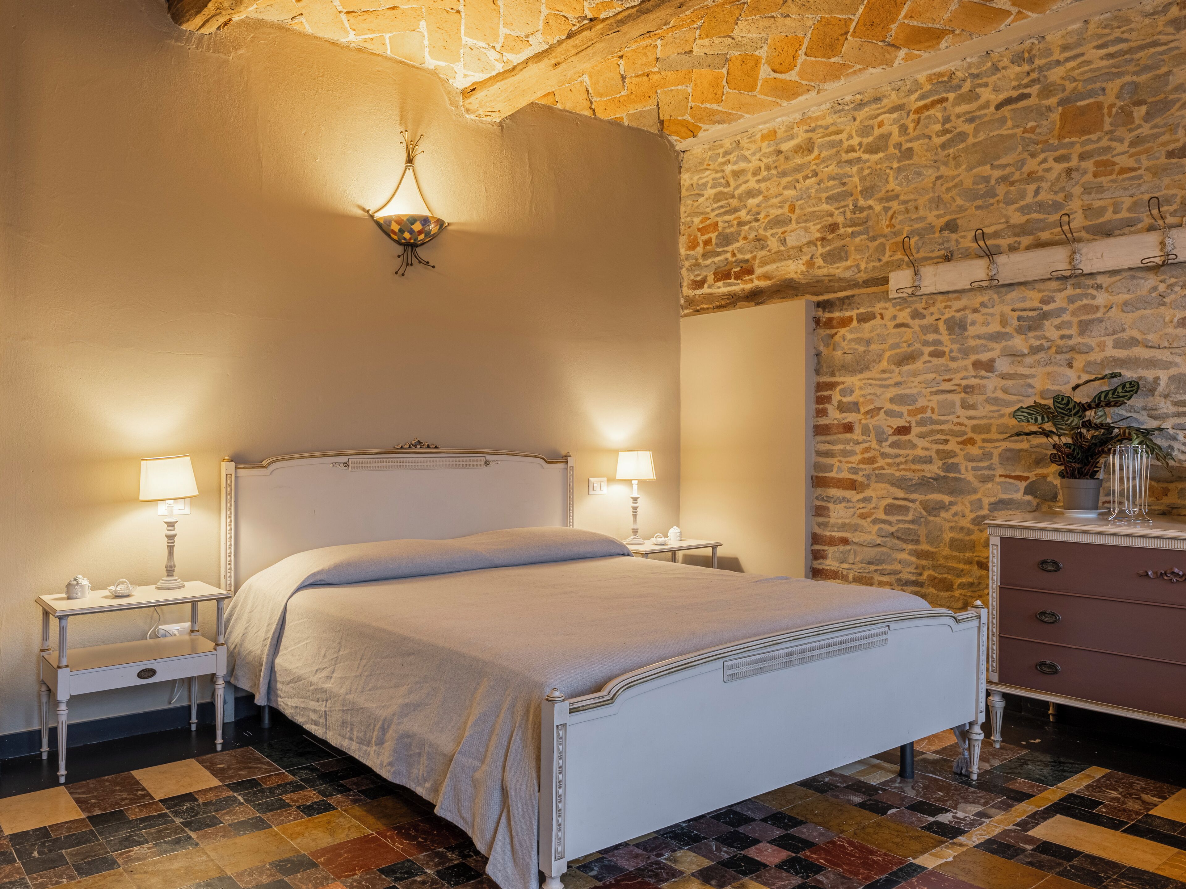 Un dormitorio con una cama, dos mesitas de noche, un aparador, una lámpara de pared y una pared de piedra.