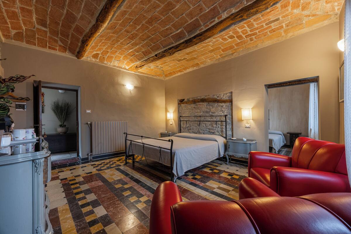Habitación de hotel con piso a cuadros, una cama, un sofá de cuero rojo, una pared de piedra y techo de ladrillo.