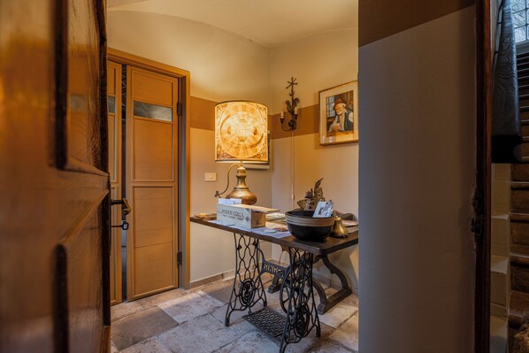 Un couloir étroit avec une porte en bois, une table sur laquelle se trouve une lampe, et un tableau encadré accroché au mur.