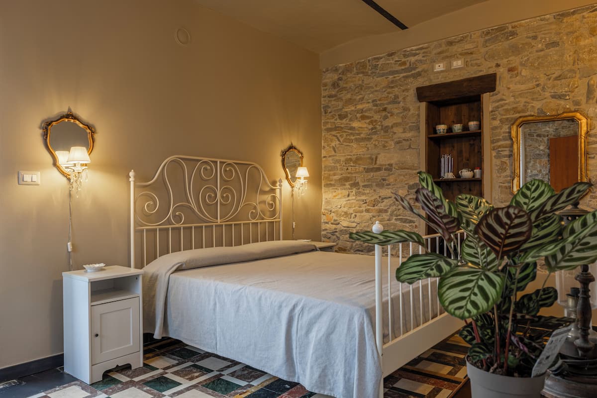 Un dormitorio con cama, mesita de noche, lámparas de pared, una pared de piedra y una planta en maceta.