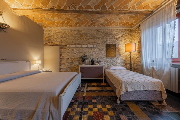 A room with two beds, a stone wall, a checkered floor, and a lamp.