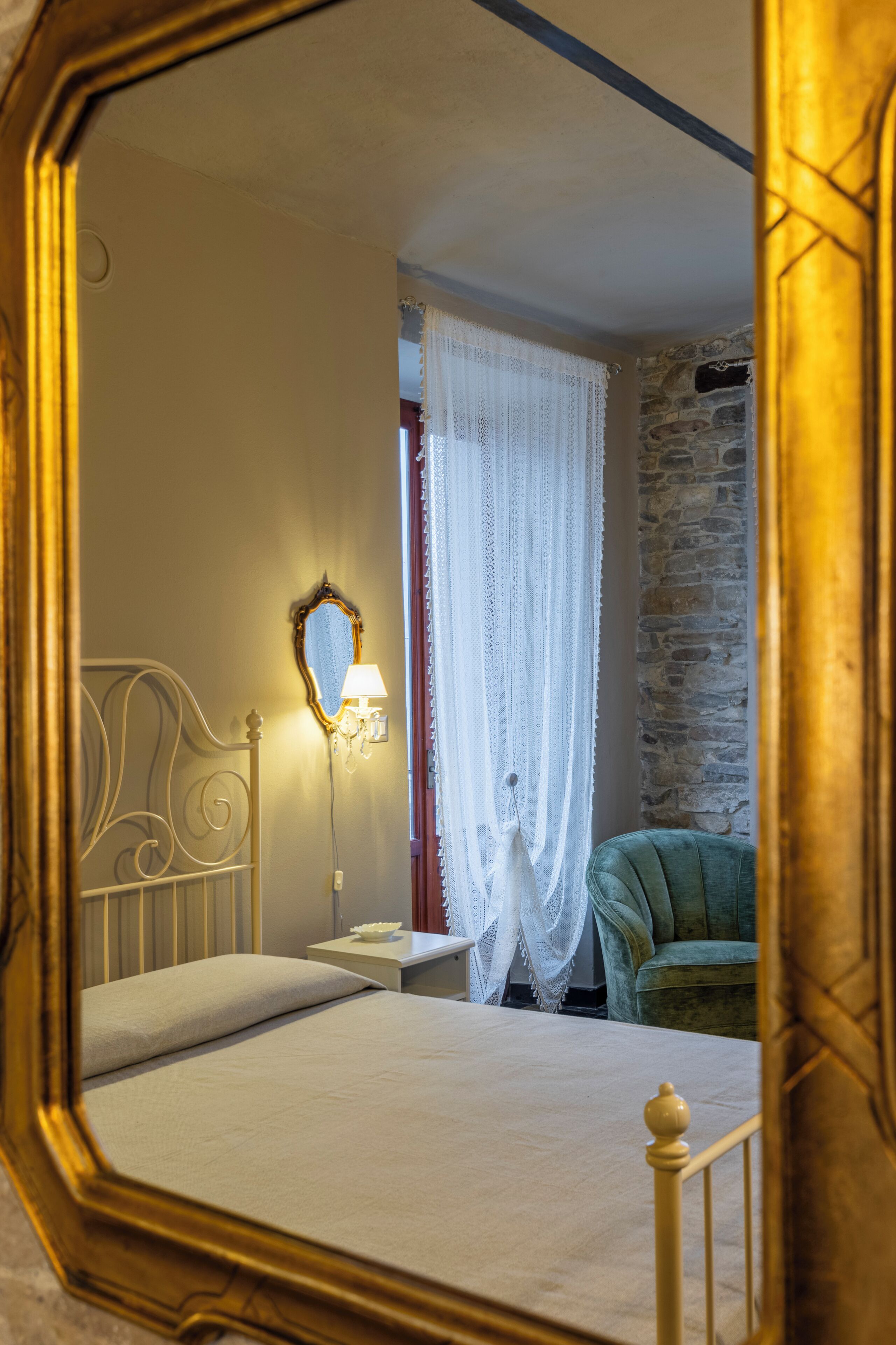 Un dormitorio con una cama, una mesita de noche, una lámpara, un espejo y un sillón verde.