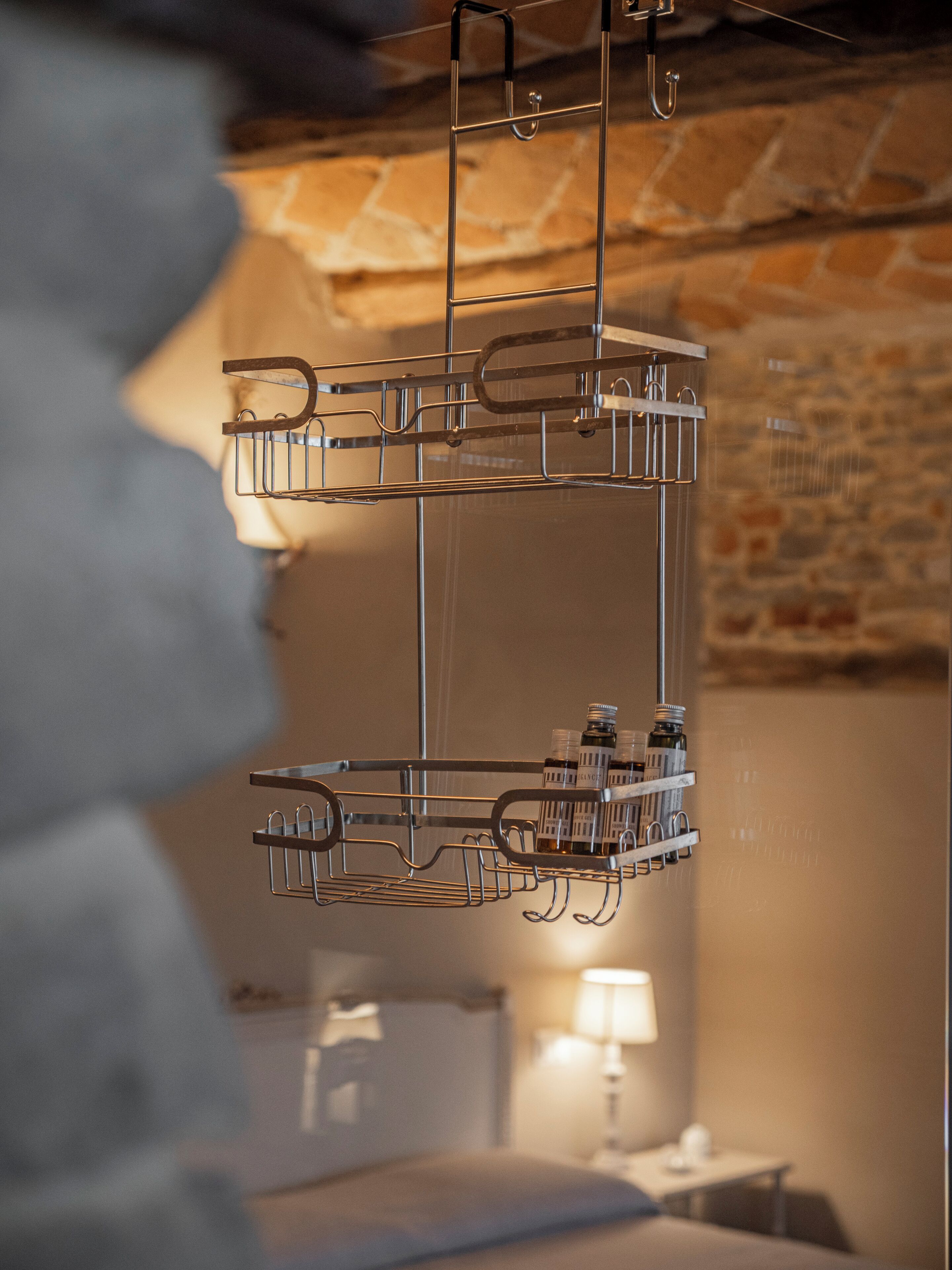 Een metalen plank met flessen en glazen, waarschijnlijk voor een minibar, in een kamer met een bakstenen muur en een bed.