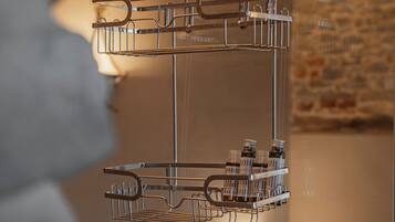 A metal rack with bottles and glasses, likely for a minibar, in a room with a brick wall and a bed.