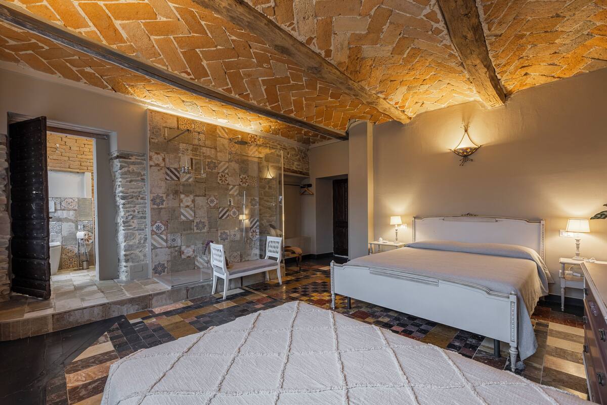 Un dormitorio con techo de ladrillo, una cama grande, dos mesitas de noche con lámparas y un suelo estampado.