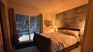 Un dormitorio con una cama de madera, una mesita de noche con lámpara y vistas a una terraza por una puerta corredera.