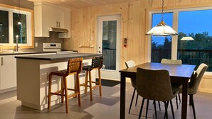 Una cocina moderna con armarios de madera, una isla central con taburetes, una mesa de comedor con sillas y un ventanal con vistas a una terraza.