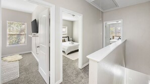 Un dormitorio moderno con cama, televisor y una puerta blanca que da a otra habitación.