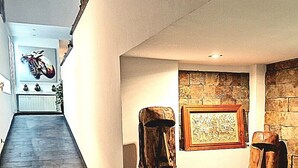 A hallway with a dark wooden floor, two wooden sculptures, a framed picture on the wall, and a stone wall.