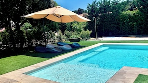 A rectangular swimming pool with a tiled edge, surrounded by a well-maintained lawn and a large umbrella providing shade.