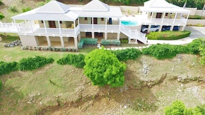 A large, multi-story house with a swimming pool, surrounded by lush greenery and a hilly landscape. - A Yacht Haven (Christiansted)